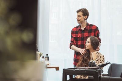 Stylist barber styling long hair for beautiful asian young woman in beauty salon, working moment