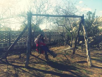 Man sitting on swing against bare trees