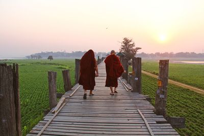 Rear view of friends walking on wood against sky during sunset