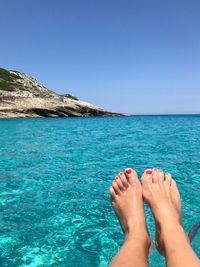 Low section of woman relaxing on blue sea against clear sky