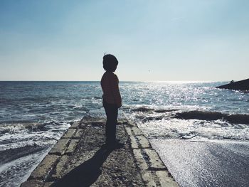 Rear view of boy walking on the beach against clear sky 