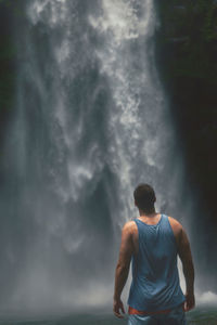 Rear view of man standing by waterfall