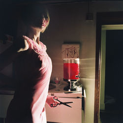 Woman wearing mask while holding scissors standing at home