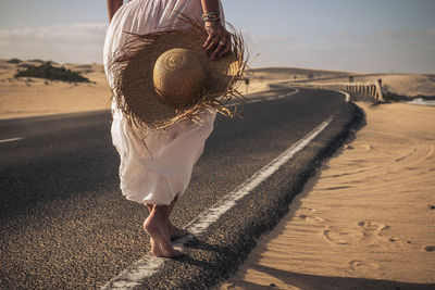 Low section of woman walking on roadside against sky