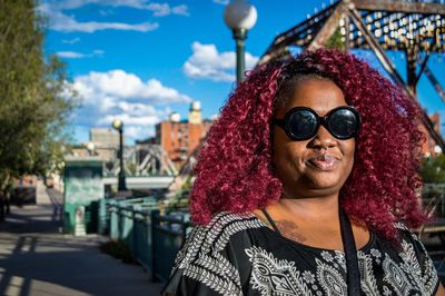 Portrait of woman with curly maroon hair while wearing sunglasses on promenade