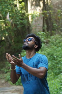 Young man wearing sunglasses standing against trees