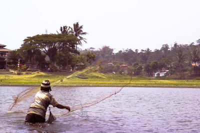 Man in lake against trees against clear sky