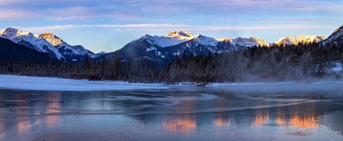 Scenic view of lake by snowcapped mountains against sky during sunset