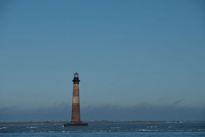 Lighthouse by sea against clear sky