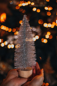 Female hands holding silver tiny christmas tree. magic cozy details, golden bokeh lights