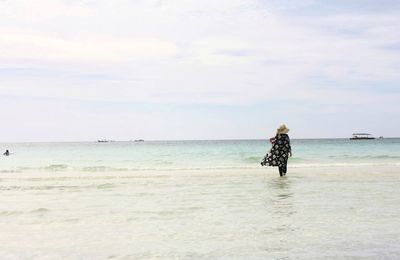 Rear view of woman standing at beach against sky