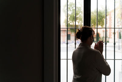 Rear view of woman looking through window at home