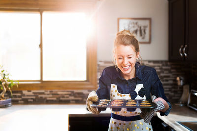 Smiling young woman holding baking sheet in kitchen at home