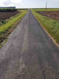 Road by agricultural field against sky