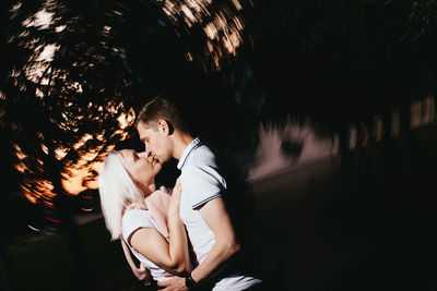 Couple kissing while standing trees at dusk