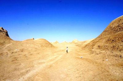 Rear view of man walking in desert against clear blue sky