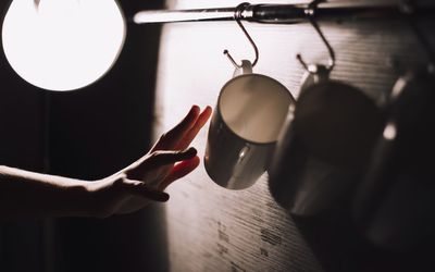 Close-up of human hand reaching towards coffee cup in darkroom