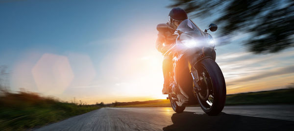 Man riding motorcycle on road against sky during sunset