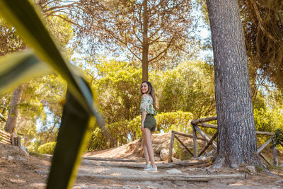 Woman standing by tree trunk in forest