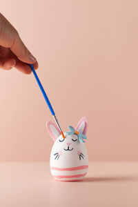 Cropped hand of woman holding piggy bank against pink background