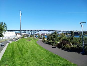 Road by bridge against clear blue sky in city