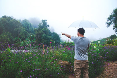 Rear view of man with arms raised standing against trees