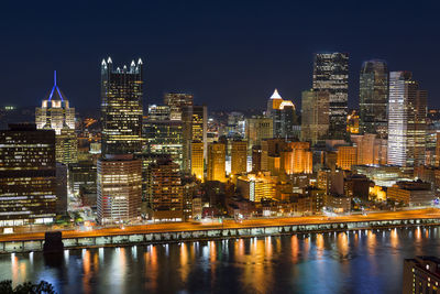 Illuminated buildings by river against sky at night