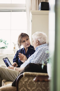 Senior man talking to caretaker while using digital tablet at nursing home