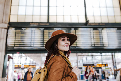 Smiling woman looking away while standing at railroad station platform