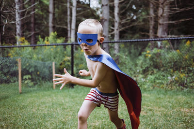 Playful shirtless boy wearing cape and eye patch while playing in yard