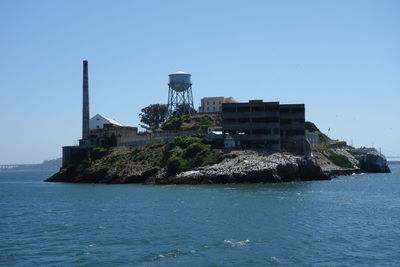 Buildings by sea against clear blue sky