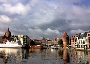 Buildings at waterfront against cloudy sky