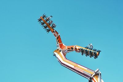 Low angle view of people enjoying at fairground ride against clear blue sky