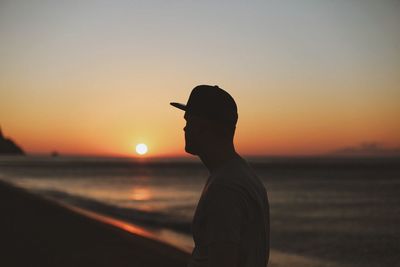 Side view of man standing on shore at beach against sky during sunset