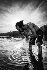 Portrait of young man standing by lake against sky