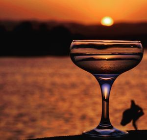 Close-up of wineglass on table against orange sunset sky