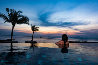 Rear view of woman in swimming pool on beach against sky during sunset