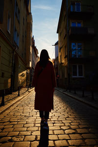 Rear view of woman walking at city street with sunset