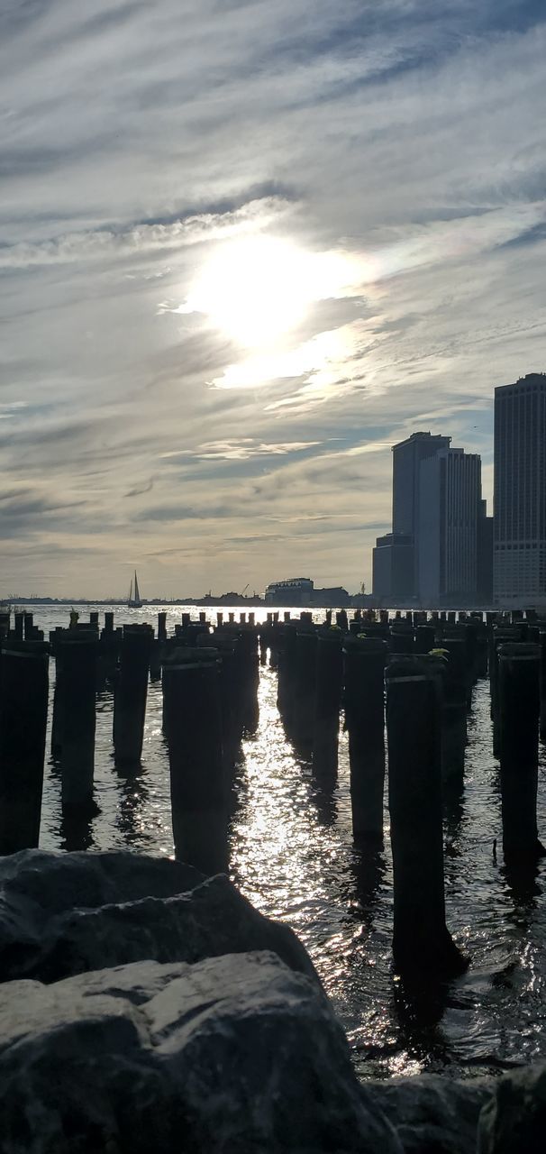 water, sky, architecture, built structure, sea, city, cloud - sky, nature, building exterior, sunset, sunlight, no people, waterfront, reflection, outdoors, scenics - nature, building, urban skyline, office building exterior, cityscape, skyscraper, wooden post, financial district