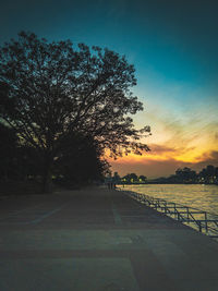 Empty road by trees against sky during sunset