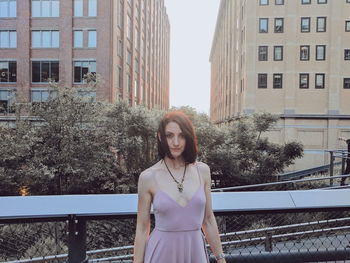 Portrait of young woman standing against building in city