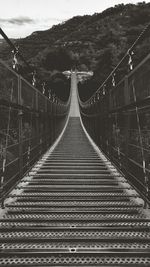 Footbridge leading towards mountain against sky