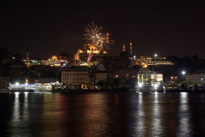 Illuminated city by river against sky at night