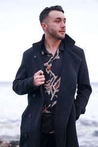 Young man looking away while standing by sea against sky