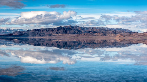 Scenic view of mountain range by lake against cloudy sky