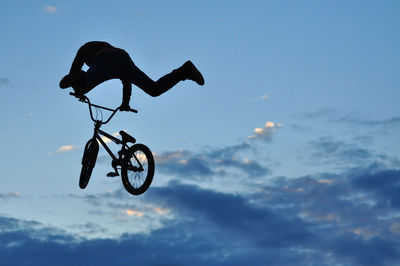 Low angle view of silhouette man with bicycle against sky