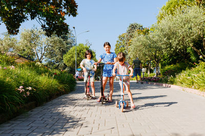 Riding scooters two smiling girl on a sunny day