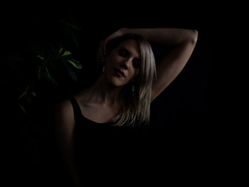 Portrait of young woman looking away against black background