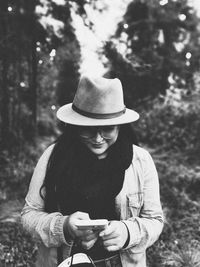 Young woman wearing hat using smart phone against trees in forest