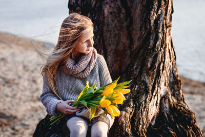 Midsection of woman holding flower on tree trunk